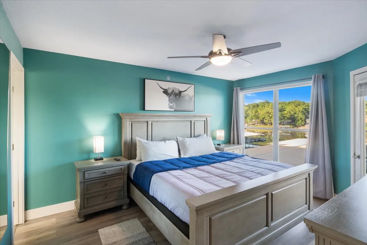 A serene bedroom featuring a comfortable bed positioned near a window, with tranquil lake views visible outside. Tasteful artwork adorns the wall, and the room is bathed in gentle natural light, creating a peaceful retreat.