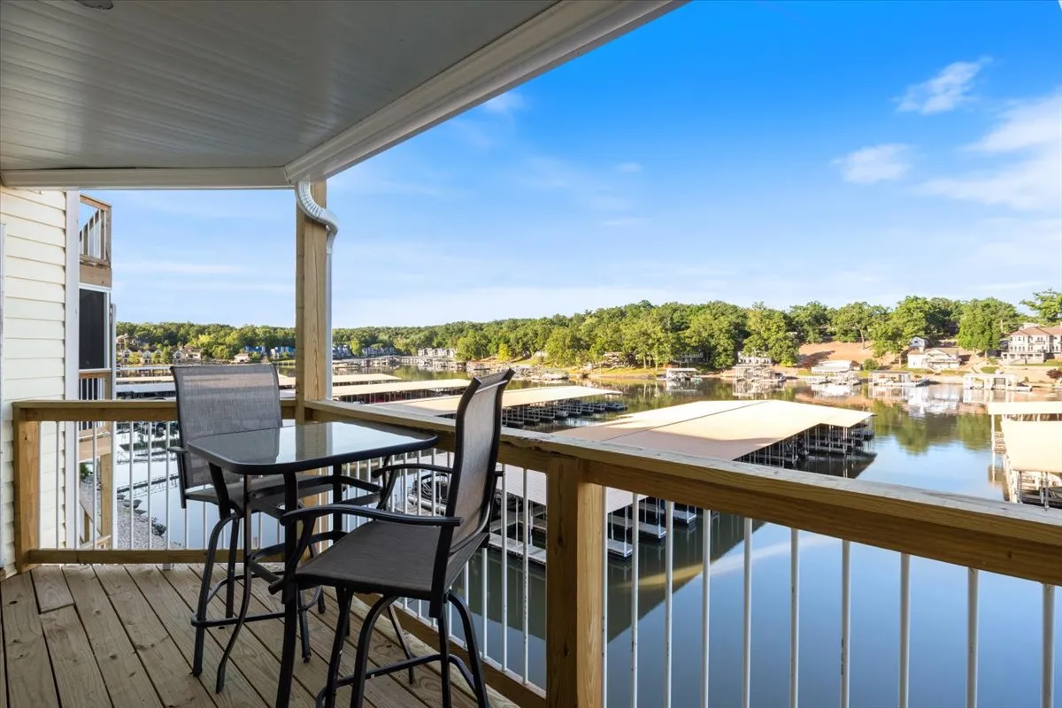 This image captures a serene balcony seating area overlooking the lake and marina. Comfortable chairs offer a perfect spot to relax with a beverage while enjoying the expansive water views. The peaceful ambiance is enhanced by the morning light or the golden glow of sunset reflecting off the water.