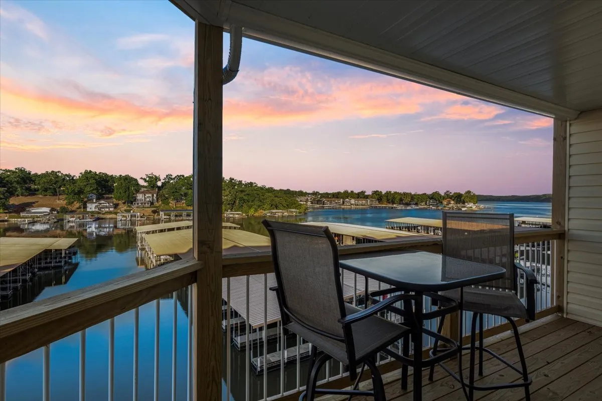 The hero image captures a serene balcony setting overlooking the main channel of Lake of the Ozarks at sunset. A table and chairs invite guests to relax and dine outdoors, with sweeping water views and a tranquil sky painting the perfect backdrop for unwinding and socializing.