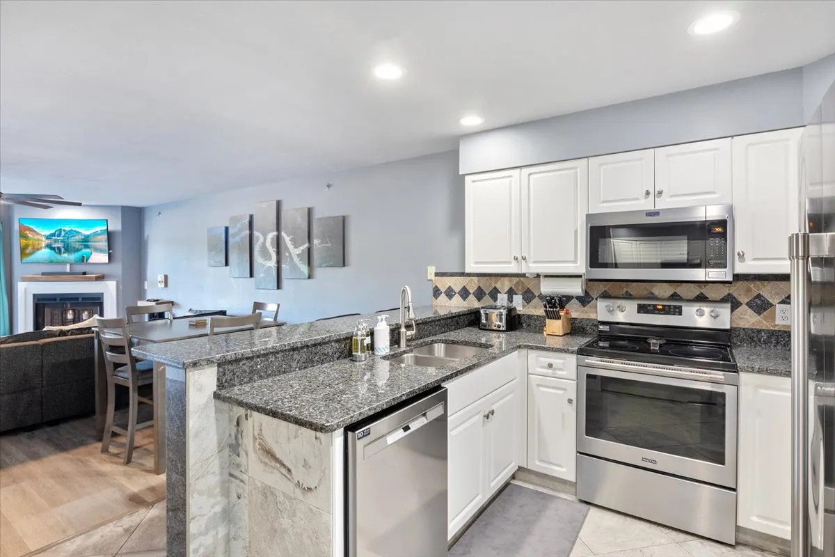 A modern kitchen featuring granite countertops, stainless steel appliances, a spacious dining area, and tasteful artwork on the walls. The open layout invites gathering and conversation, with plenty of seating for casual meals or special celebrations.