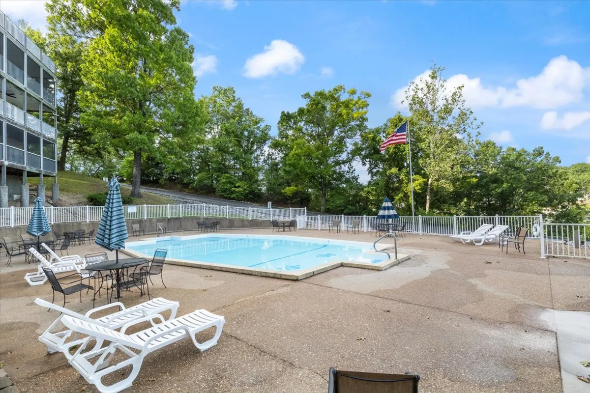 A sparkling resort-style swimming pool surrounded by comfortable lounge chairs and vibrant greenery. The American flag adds a welcoming community touch, while the pool area is bathed in inviting natural light, suggesting an ideal spot for swimming, sunbathing, and social gatherings.