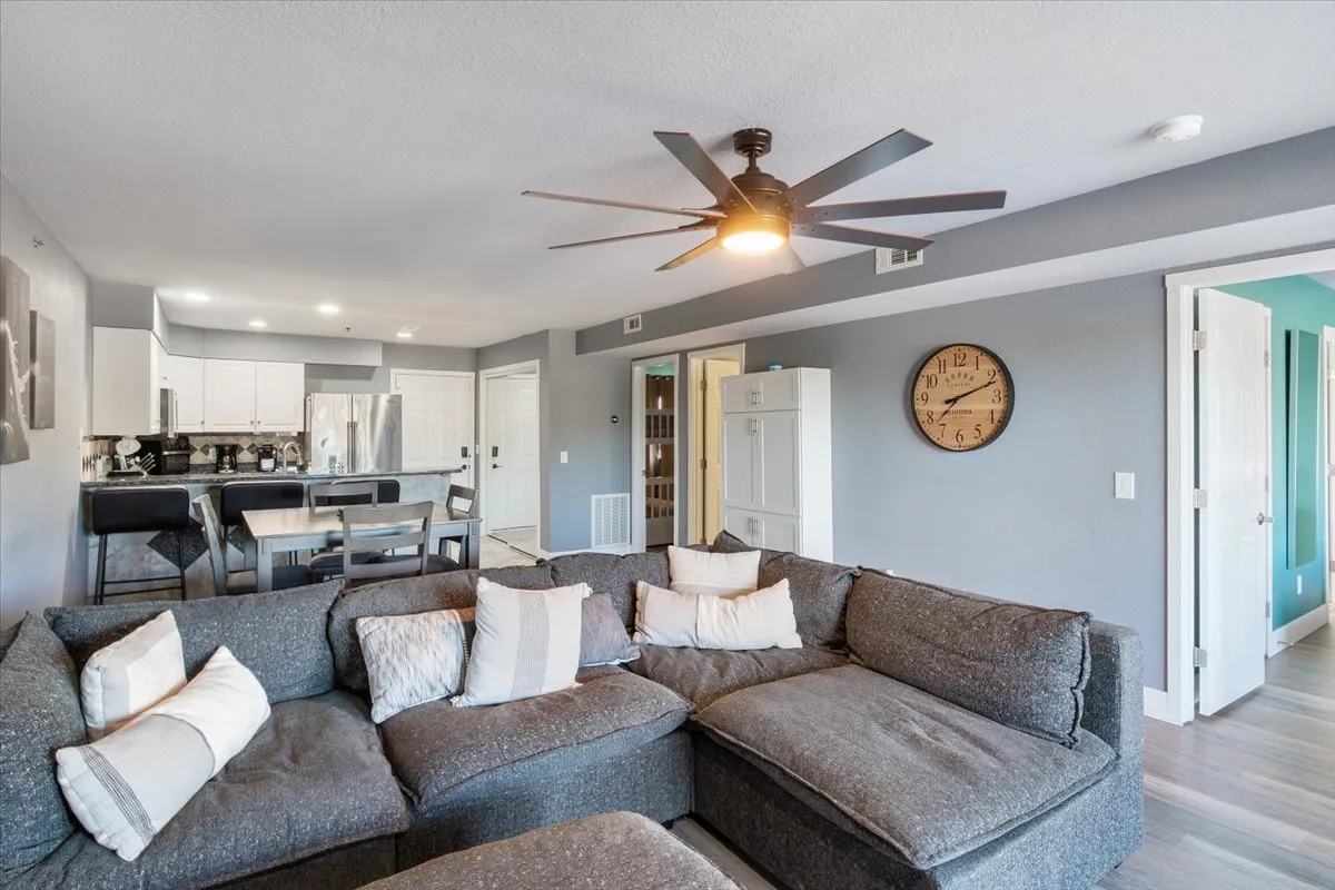 A spacious living room with a large sectional sofa, adjacent kitchen area, and dining table. The room is styled for relaxation and social gatherings, with plush seating and a cozy, welcoming mood.